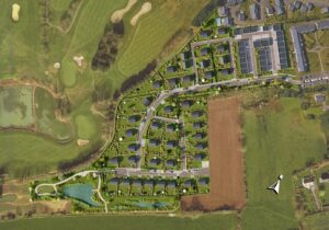 Vue aérienne d’un quartier résidentiel verdoyant à Port-en-Bessin-Huppain, avec terrain de golf, étang et maisons individuelles.